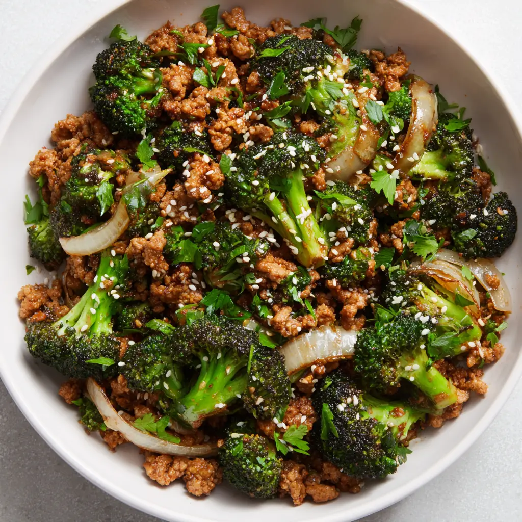 Close-up top-down view of a savory ground turkey and broccoli skillet with a slightly glossy brown sauce in a white ceramic bowl.
