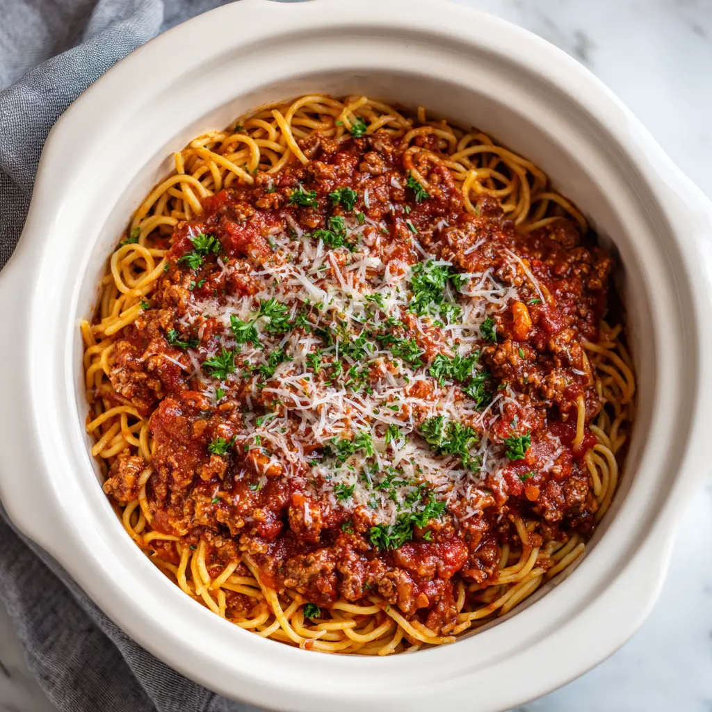 A close-up view of Crockpot Spaghetti noodles fully submerged in a hearty, dark red tomato-based meat sauce with visible chunks of ground beef.