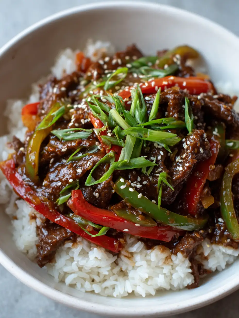 A top-down close-up shot of tender simmered beef strips in a thick dark glossy sauce, part of a Slow Cooker Pepper Steak recipe.