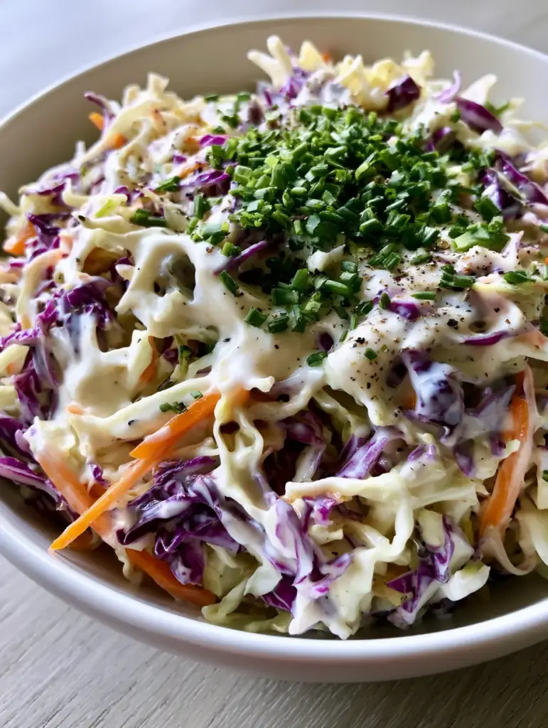 Close-up of a Homemade Coleslaw Recipe in a white ceramic bowl with thick creamy dressing and fresh chives.