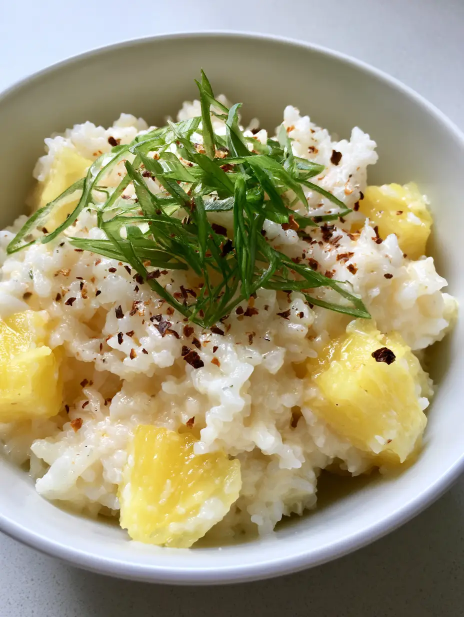A close-up handheld smartphone photo of a white ceramic bowl filled with creamy Coconut Pineapple Rice mixed with large chunks of bright yellow pineapple.