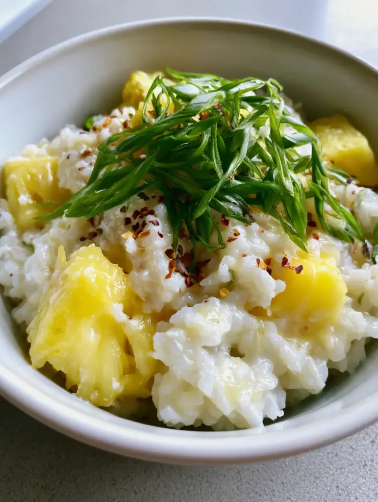 Coconut Pineapple Rice served in a white bowl on a light grey countertop, showcasing the fluffy texture and colorful scallion garnish.