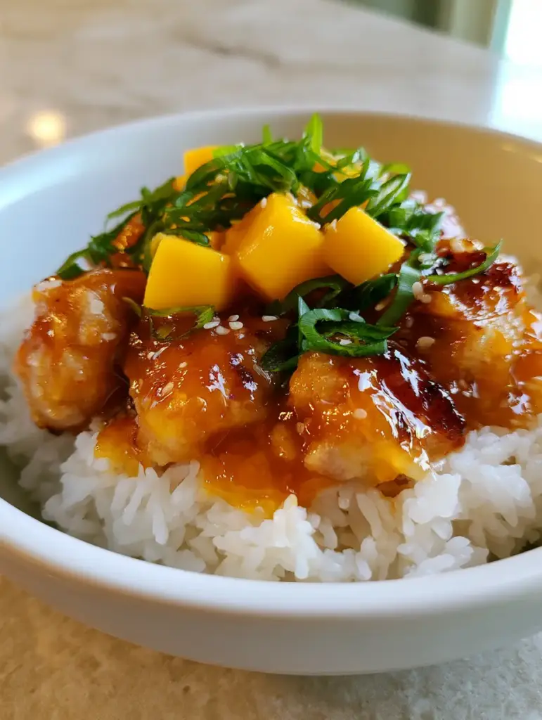 Overhead view of Mango Glazed Chicken with fresh rectangular mango cubes and bright green scallion garnish.