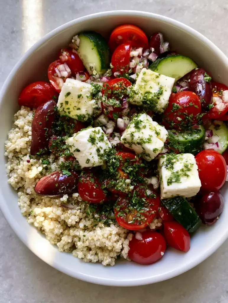 Top-down view of a Mediterranean Quinoa Salad showing fluffy grains, red tomatoes, and dark green cucumber skins in a white bowl.