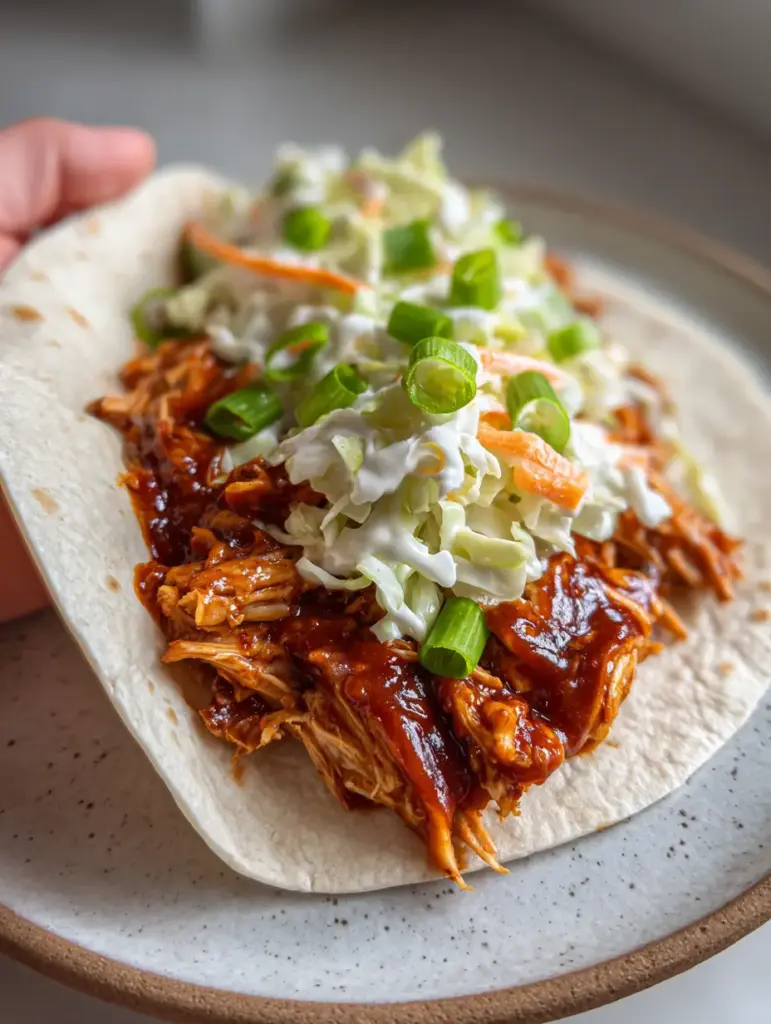 Inside look at the layers of a BBQ Chicken Coleslaw Wrap featuring glossy chicken, orange carrots, and green scallions.