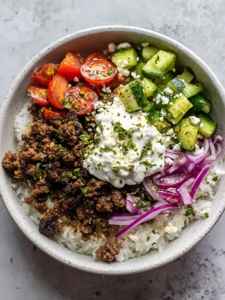 Greek Lamb Gyro Bowls with fresh diced cucumbers, red onions, and a thick dollop of tzatziki sauce.