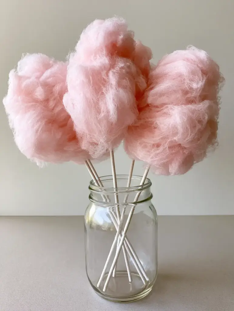 Three pink cotton candy clouds held vertically in a clear glass mason jar on a gray counter.