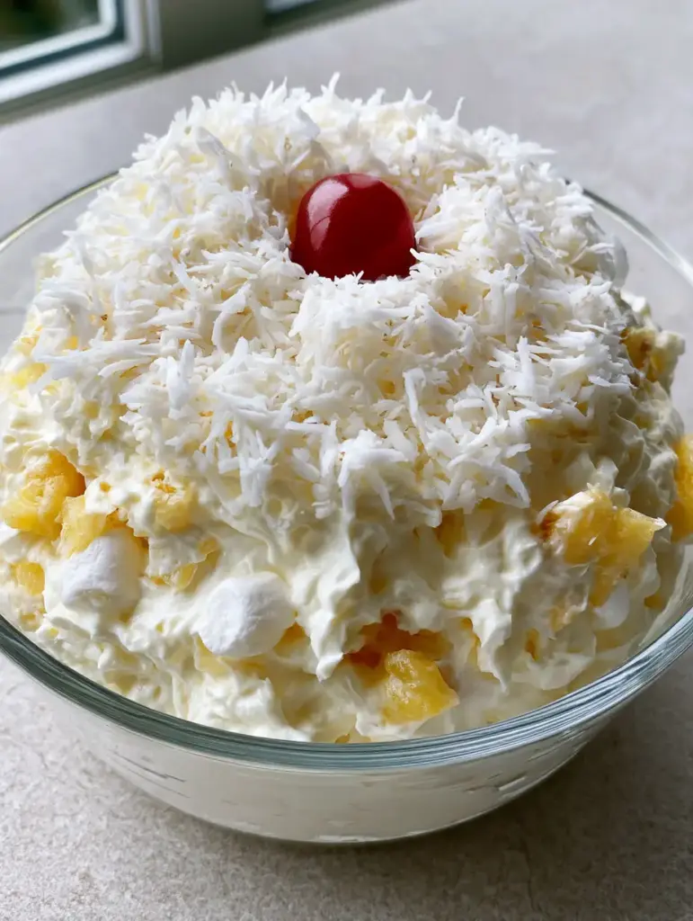 Top view of Hawaiian Pineapple Coconut Fluff heavily garnished with shredded coconut and a bright red maraschino cherry.