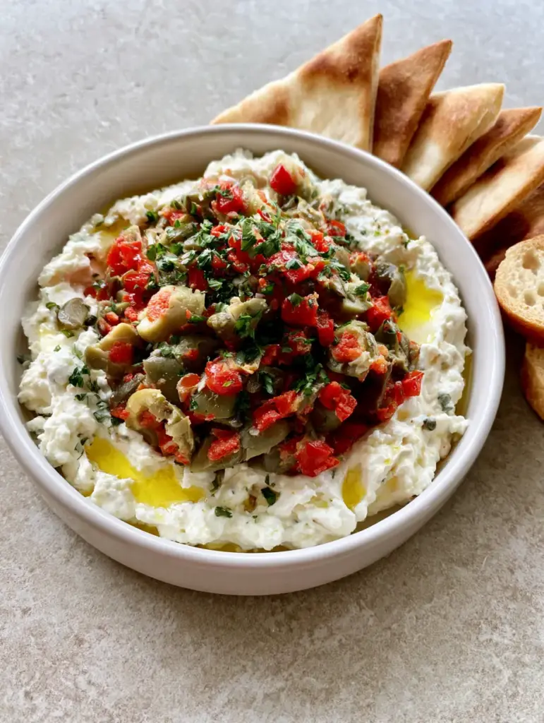 A high-angle shot of Feta and Green Olive Dip served with golden toasted baguette slices.
