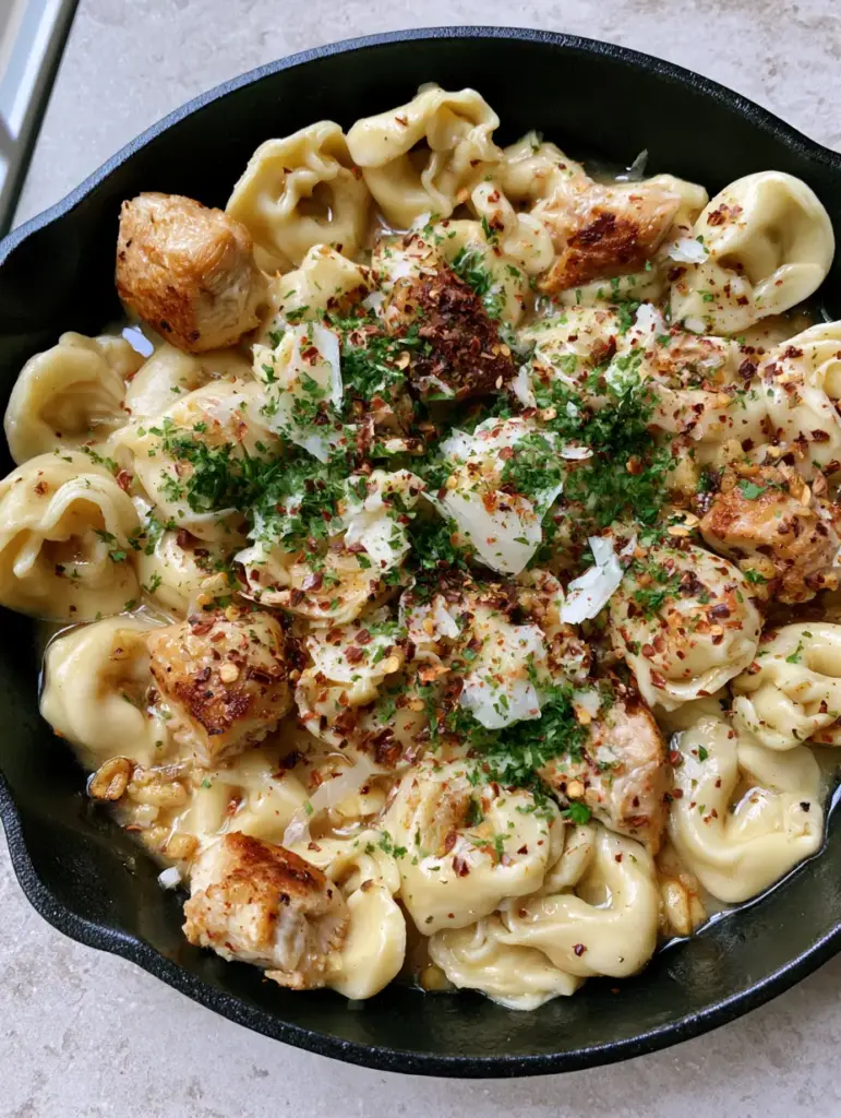 A wide shot of Spicy Garlic Butter Chicken Tortellini in a skillet on a stone countertop with natural side lighting.