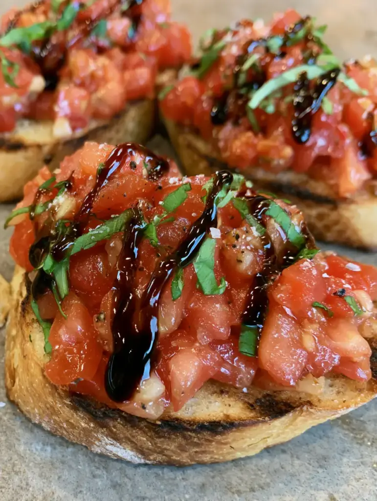 Toasted baguette slices with char marks topped with tomatoes and balsamic glaze for an Authentic Italian Bruschetta.